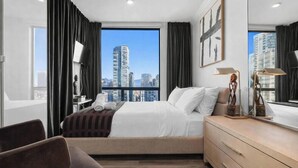 Moderni hotellihuone, jossa on suuri sänky, työpöytä, tuoli ja näkymä kaupungin ylle.