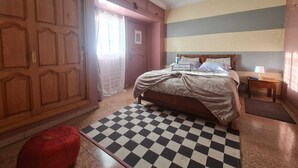 Ein Schlafzimmer mit kariertem Boden, einem Bett, einem Kleiderschrank, einem Nachttisch und einer Pendelleuchte.