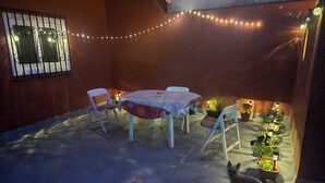 Eine Terrasse im Freien mit Tisch, Stühlen, Lichterketten und Blumentöpfen.