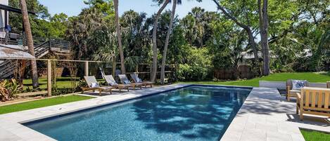 A rectangular swimming pool with lounge chairs and a wooden deck.