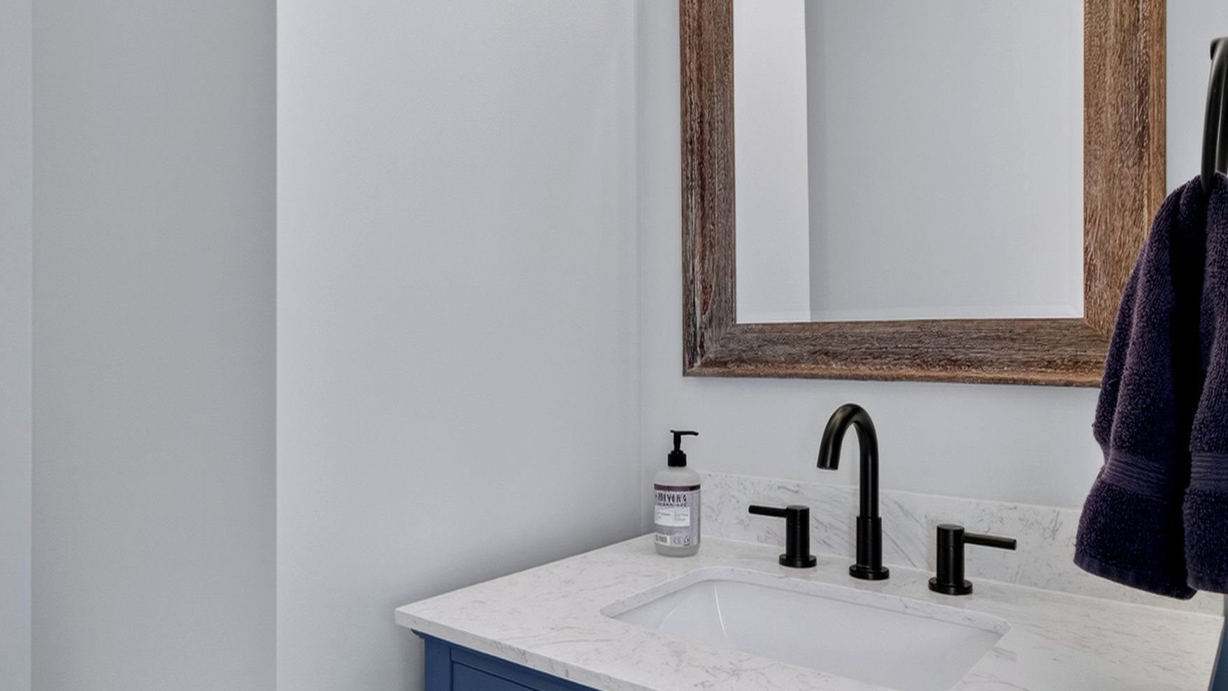 A bathroom with a white marble sink, black faucet, and a wooden-framed mirror.