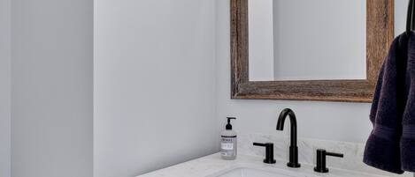 A bathroom with a white marble sink, black faucet, and a wooden-framed mirror.