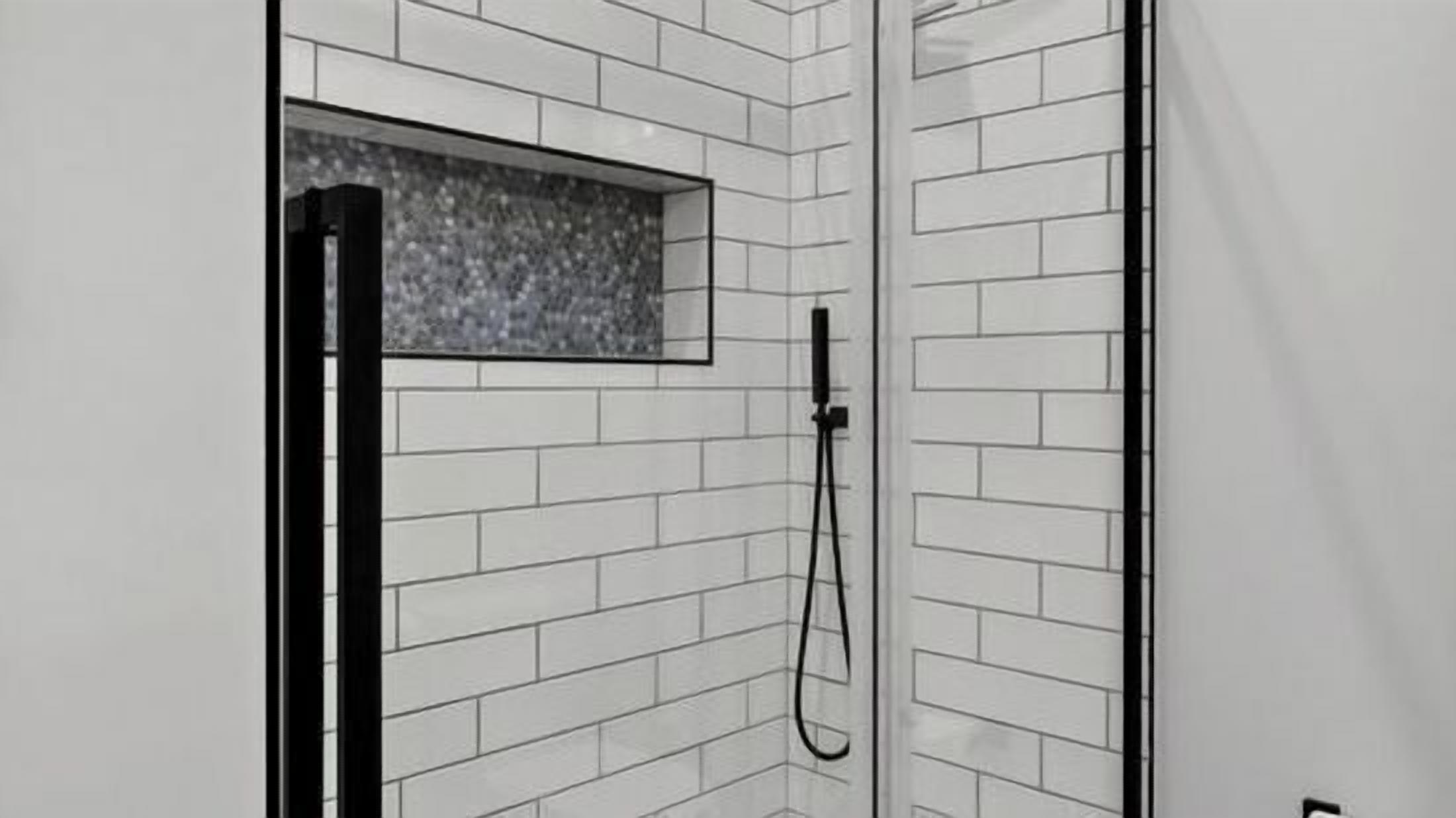 A shower with white tiled walls and a black showerhead.
