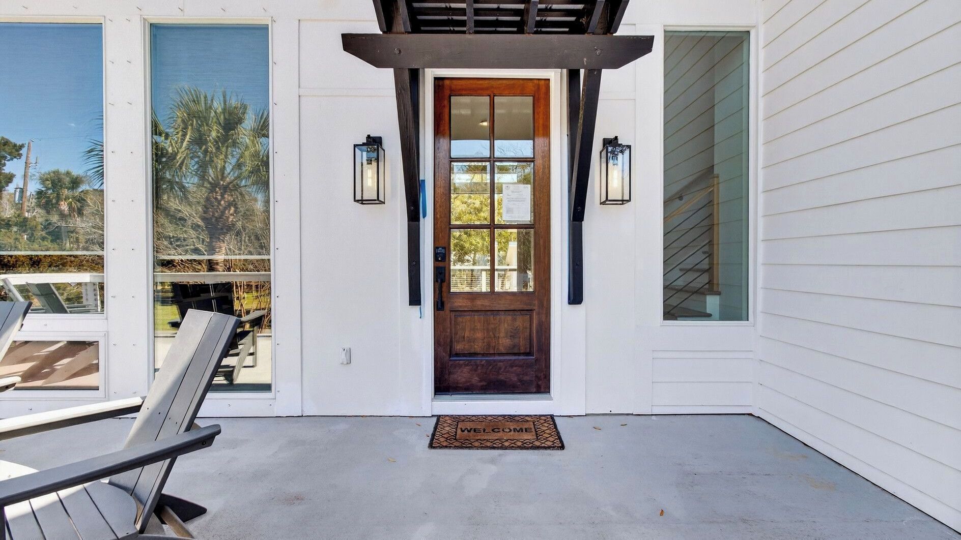 A house entrance with a wooden door, a welcome mat, and two wall-mounted lanterns.