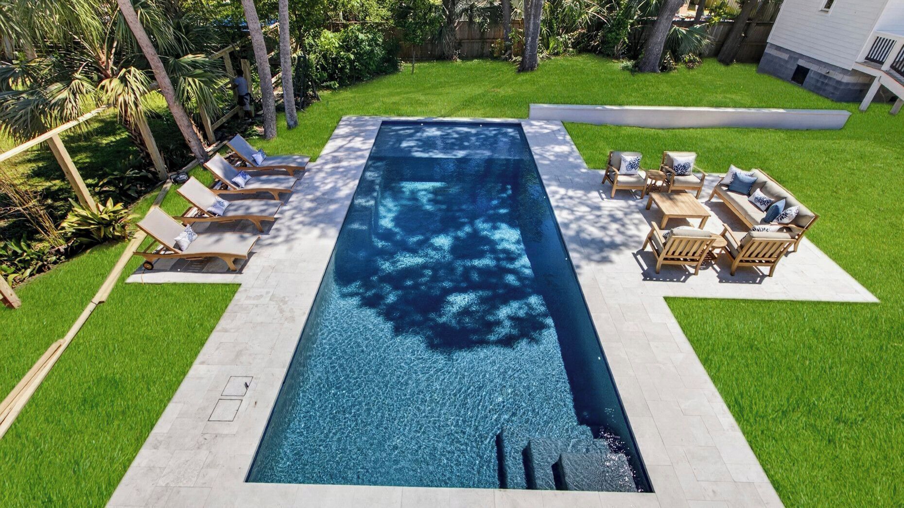 A rectangular swimming pool with a tiled deck, surrounded by a well-maintained lawn and wooden deck furniture.