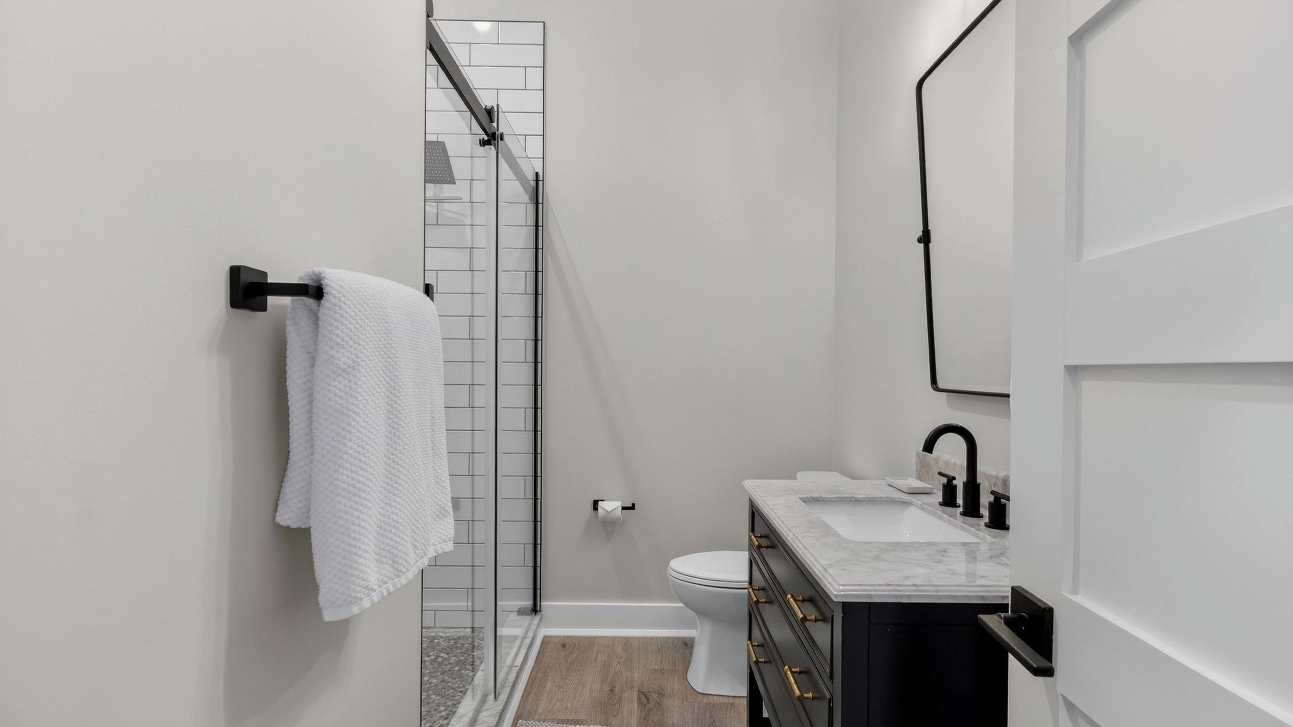 A modern bathroom with a glass shower enclosure, a white toilet, and a marble sink with black fixtures.