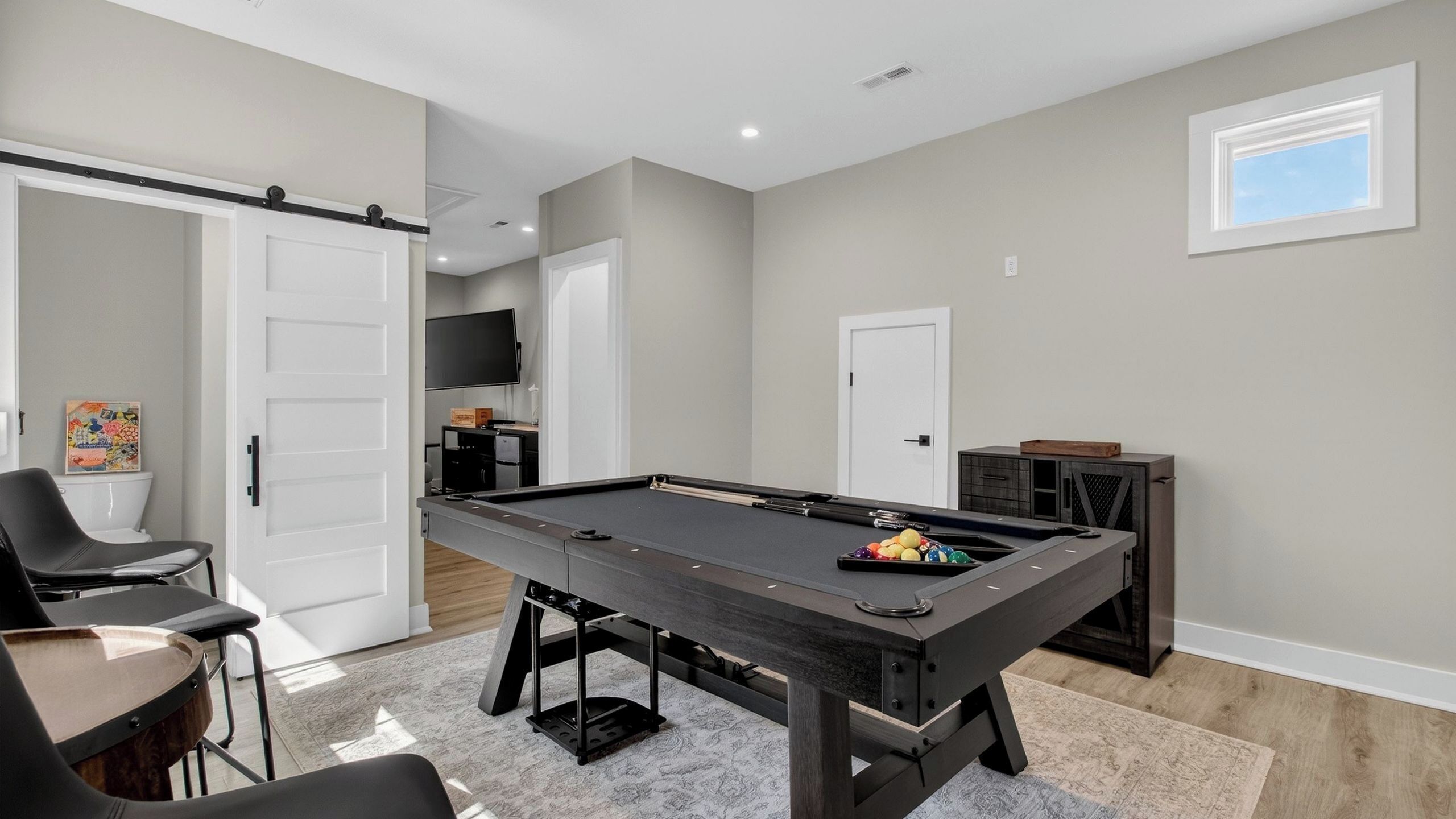 Una mesa de billar en una habitación con una puerta corredera, un televisor y un mueble pequeño.
