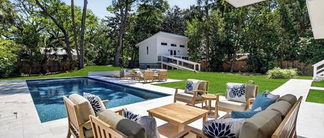 A backyard with a swimming pool, outdoor furniture, and a two-story house.