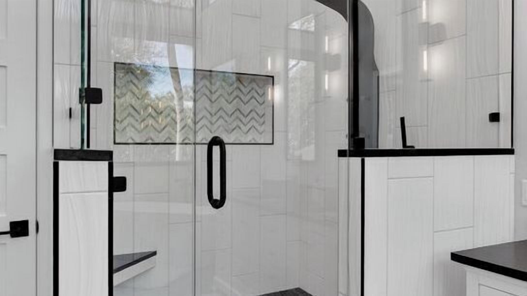 A modern kitchen with white cabinetry, a black countertop, and a glass shower enclosure with a chevron-patterned glass door.