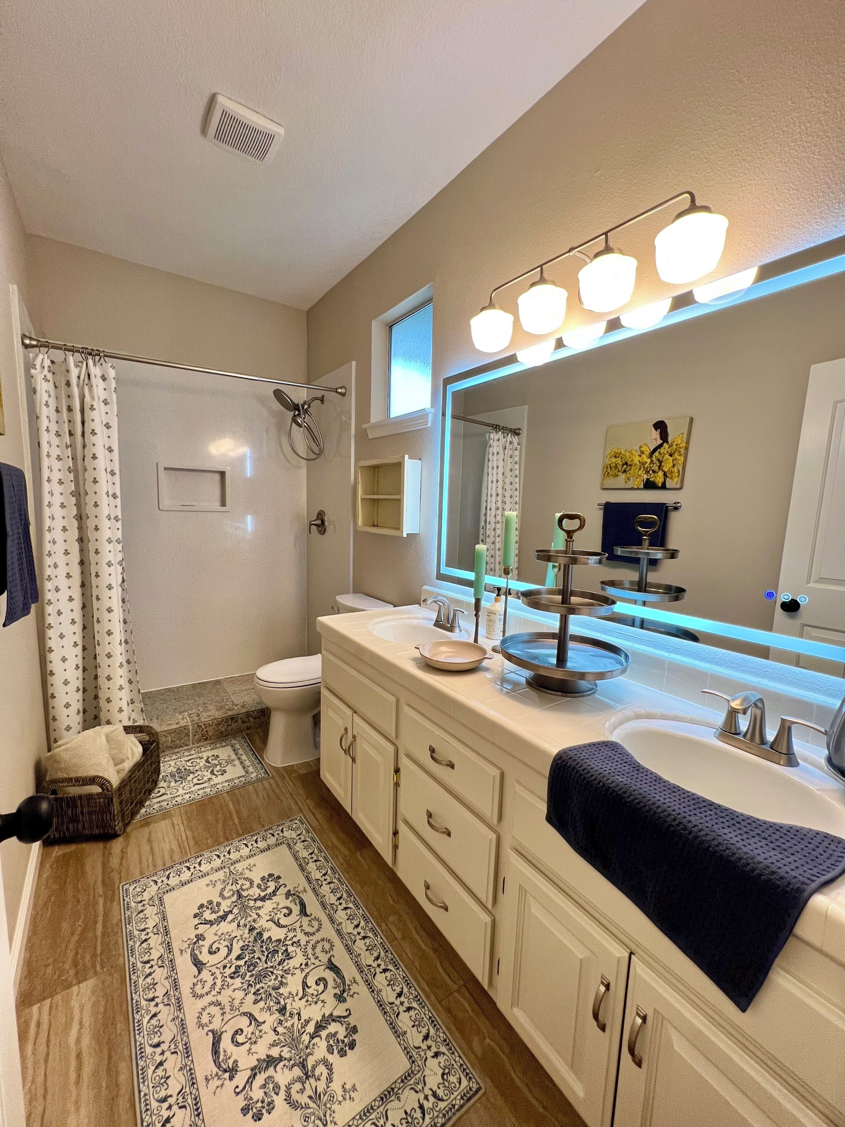 Une salle de bain avec un double lavabo, un grand miroir, une douche et un tapis à motifs.