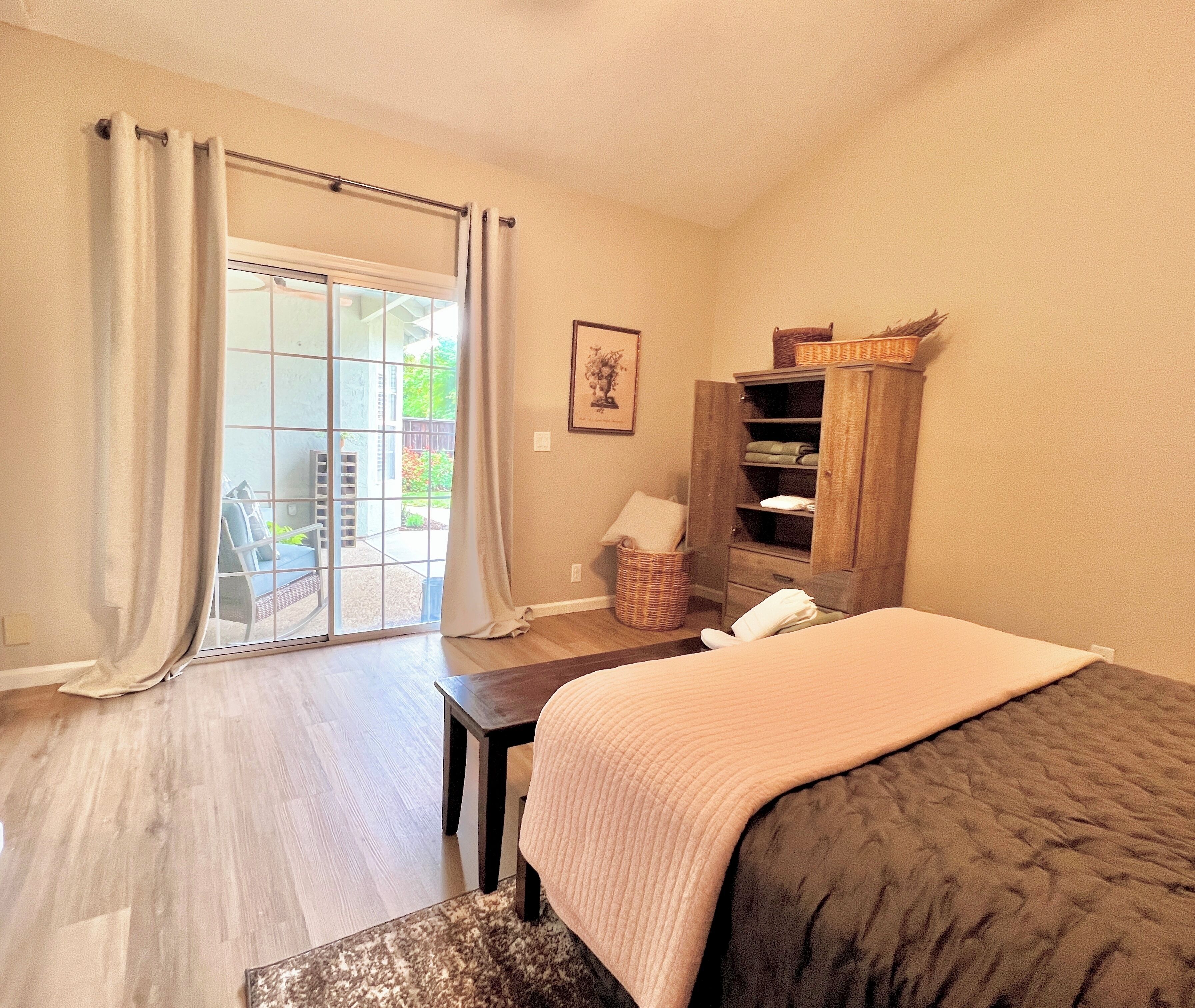 Quarto com cama, guarda-roupa de madeira, janela com cortinas e vista exterior.