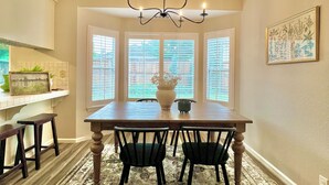 A dining area with a wooden table, four chairs, a chandelier, and a large window with blinds. - Vineyard Getaway 3BR Home in Lodi minutes away from shopping & attractions (Lodi)