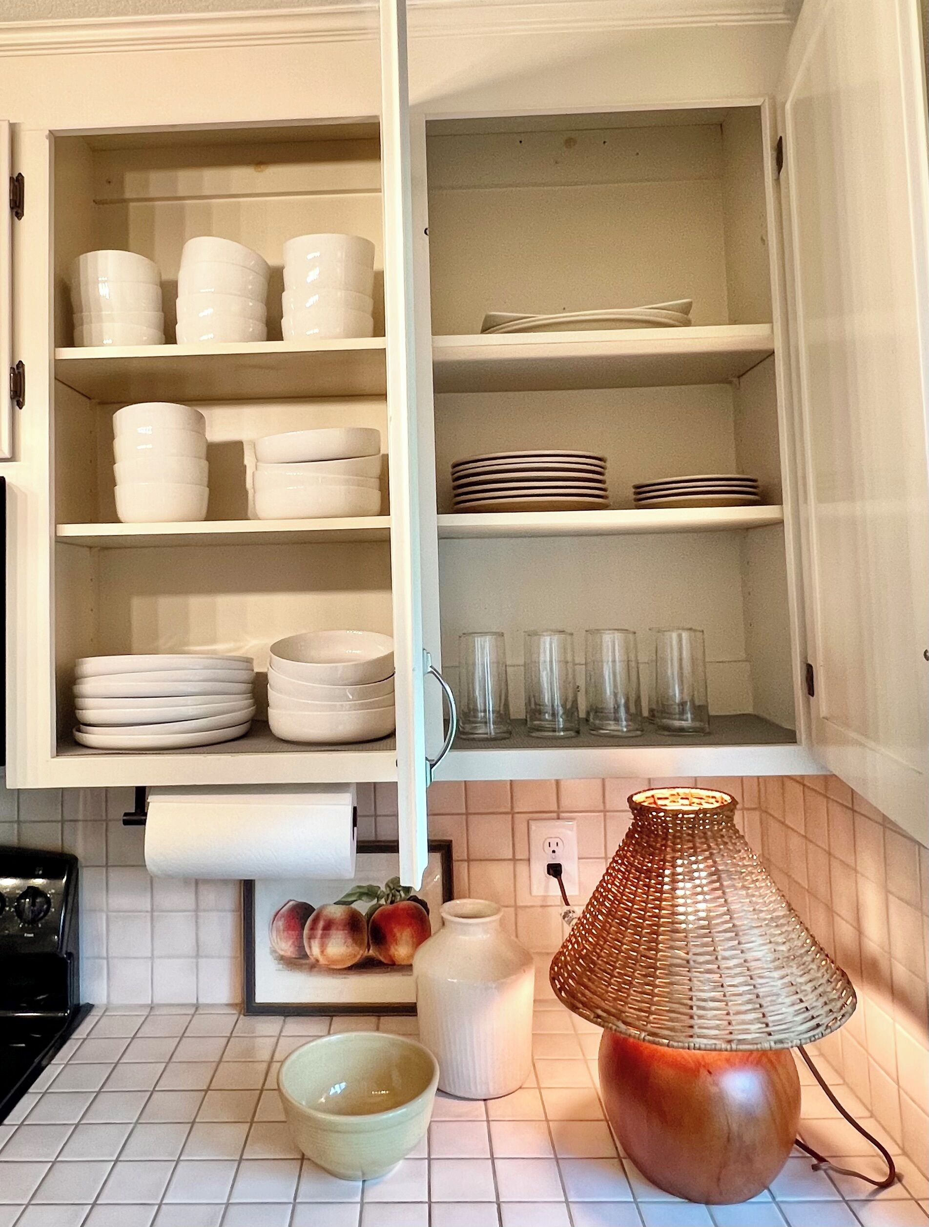 Una cocina con armarios blancos, estufa, lavamanos y lámpara de mimbre.