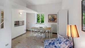 Ein Zimmer mit Esstisch, Stühlen, einer Couch, einer Lampe und einem Bild an der Wand.