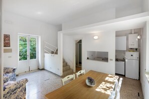 A modern kitchen with white cabinets, a wooden dining table, and a staircase leading to a second floor. - Le Tore – Frantoio Apartment with Shared Terrace, Garden, and Wi-Fi (Massa Lubrense)