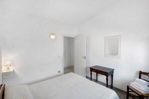 Une chambre d’hôtel comprenant un lit, un bureau, une chaise, une lampe et une porte donnant sur une autre pièce.