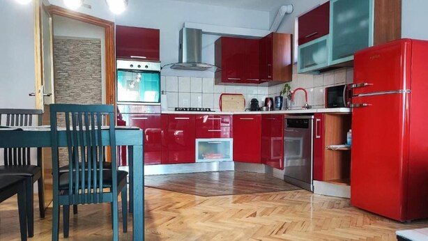 Keittiössä on punaiset kaapit, mikroaaltouuni, liesi sekä ruokailutila, jossa on pöytä ja tuolit.