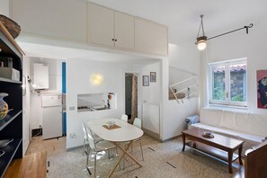 A compact kitchen with a dining area, a sofa, and a window with a view. - Le Tore – Minucciola Apartment with Shared Terrace & Garden, Wi-Fi (Massa Lubrense)