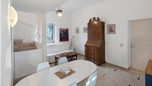 Ein Zimmer mit einem weißen Tisch, Stühlen, einem Holzschrank und einer Treppe.