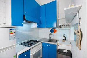 A kitchen with blue cabinets, a gas stove, a sink, and a white refrigerator. - Le Tore – Minucciola Apartment with Shared Terrace & Garden, Wi-Fi (Massa Lubrense)