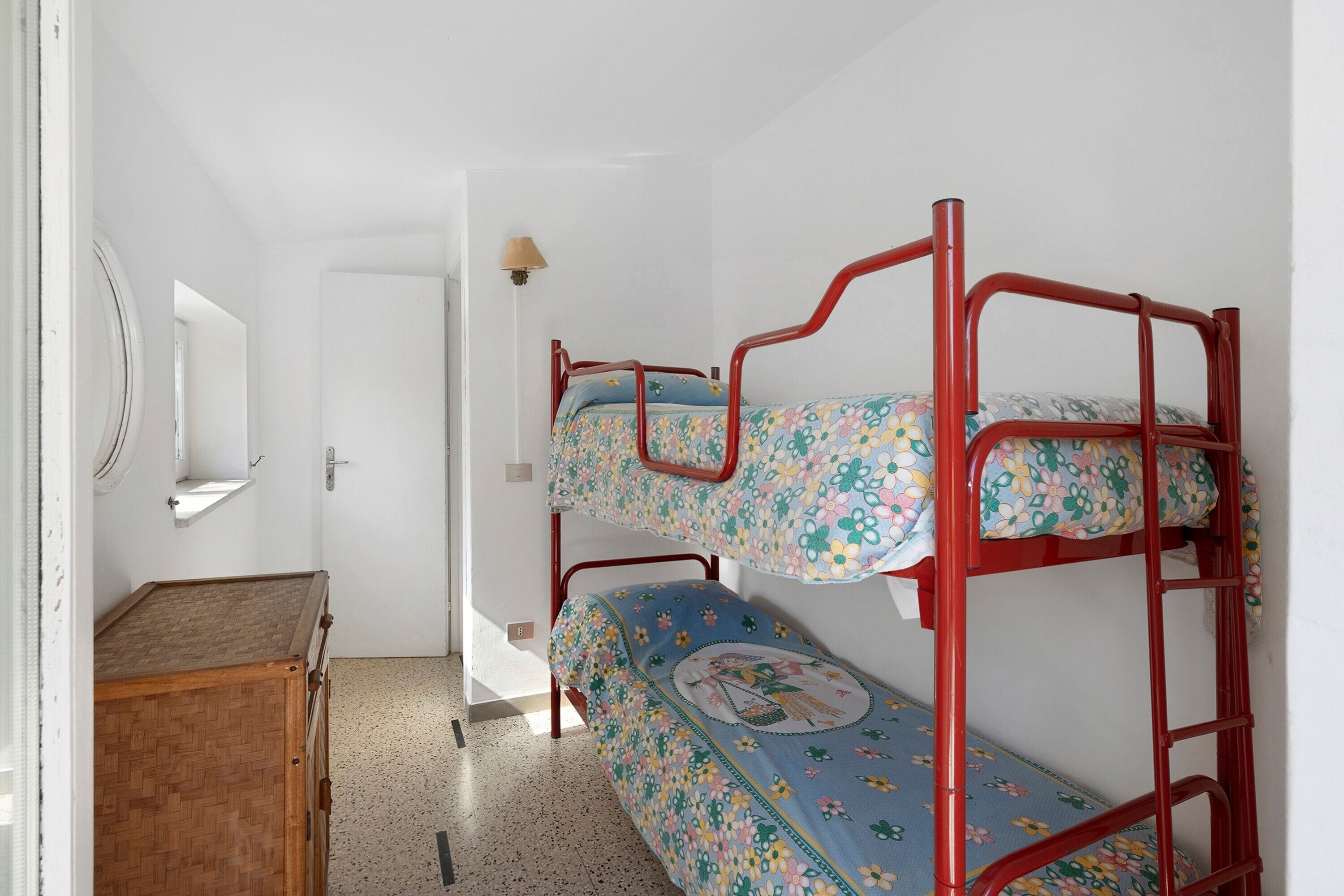 Un lit superposé avec une literie à motifs floraux, une commode en bois et un miroir au mur.