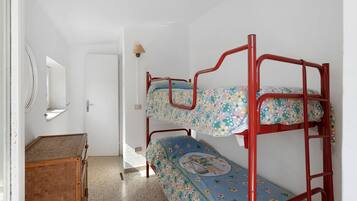 Un lit superposé avec une literie à motifs floraux, une commode en bois et un miroir au mur.