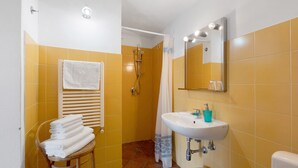 Ein Badezimmer mit gelben Fliesen, einem weißen Waschbecken, einem Spiegel, einem Handtuchhalter und einer Duschkabine.