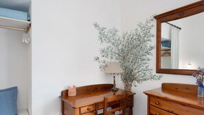 Ein Holztisch mit Schubladen, ein Stuhl, eine Lampe und ein Spiegel in einem Raum mit weißen Wänden und einer hängenden Pflanze.