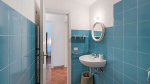 Een badkamer met blauwe tegels, een witte wasbak, een spiegel en een deur die leidt naar een andere kamer.