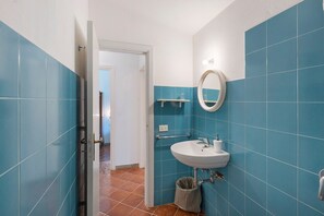 A bathroom with blue tiles, a white sink, a mirror, and a door leading to another room. - Le Tore – Palmento Room with Private Terrace, Shared Garden and Wi-Fi (Massa Lubrense)