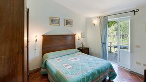 Een slaapkamer met een bed, een houten deur, een nachtkastje, een wandlamp en een raam met gordijnen.