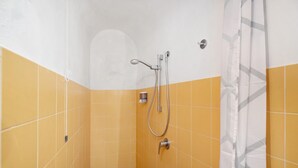 A bathroom with yellow and white tiled walls, a shower with a handheld showerhead, and a towel rack. - Le Tore – Volta 2 Room with Terrace, Shared Garden, and Wi-Fi (Massa Lubrense)