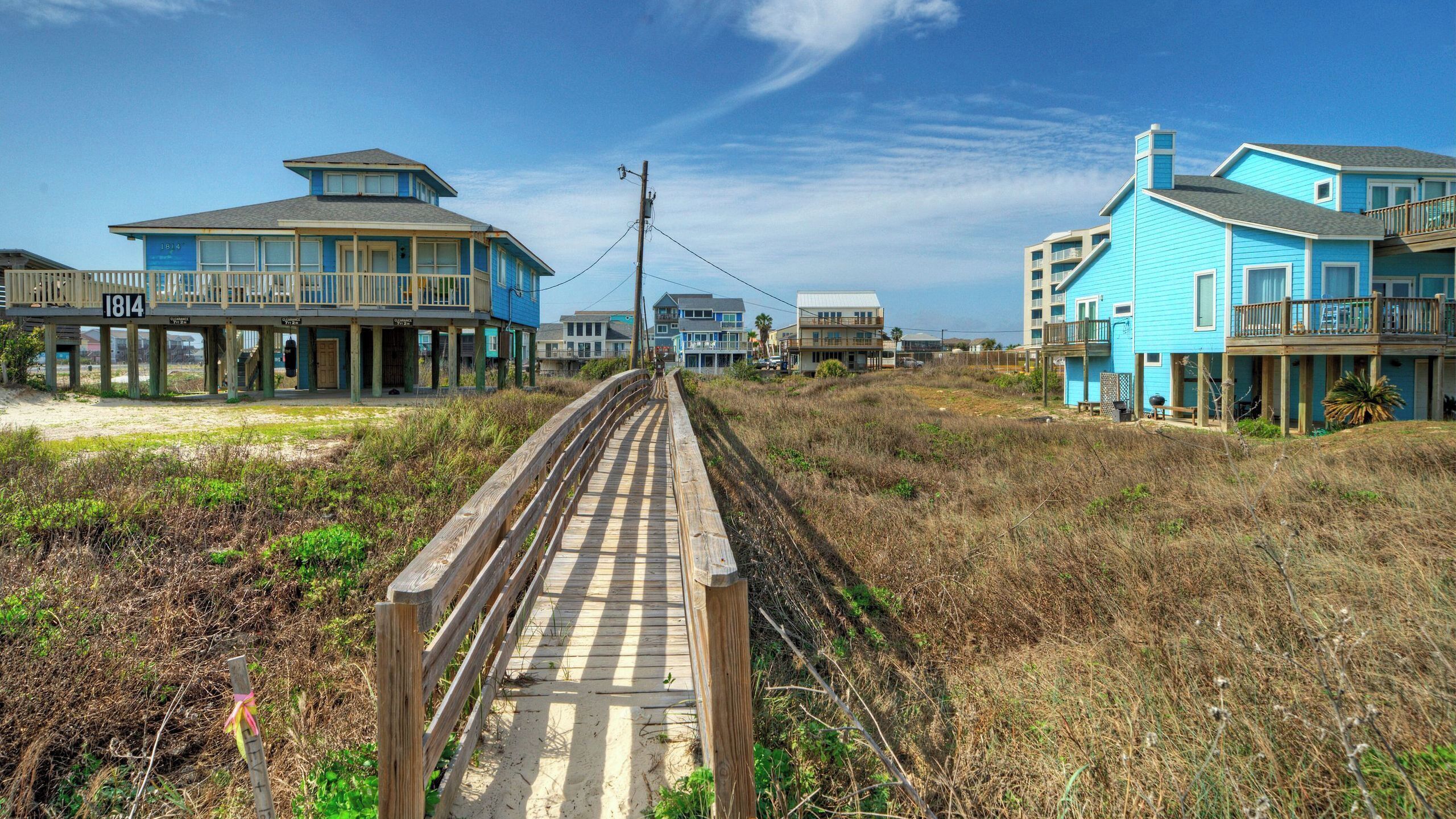 Une promenade en bois mène à des propriétés situées en bord de mer, qui comportent plusieurs étages et des balcons.