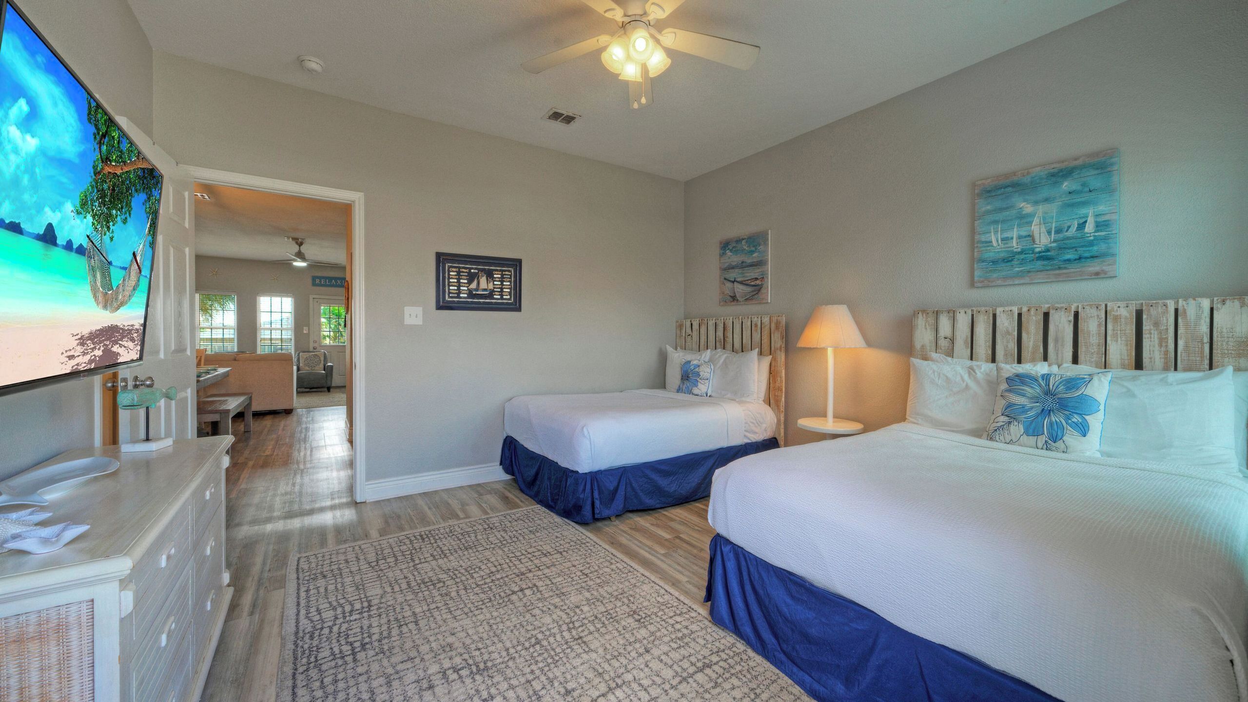 A hotel room with two beds, a TV, a ceiling fan, and a view of the outdoors.