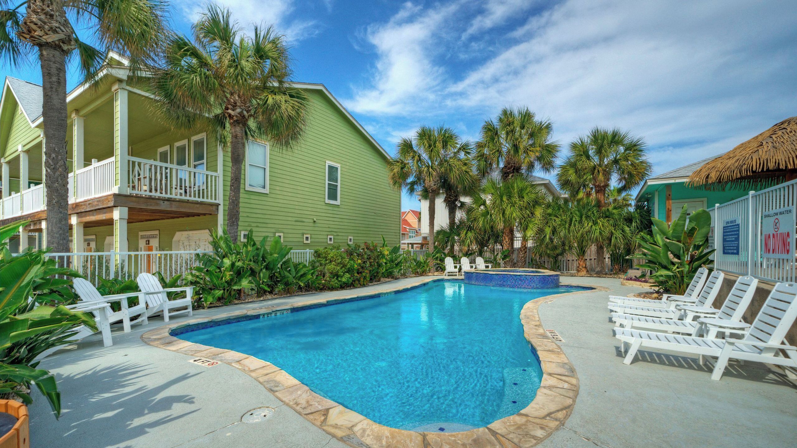 A pool area with lounge chairs, a small pool, and a building with balconies.
