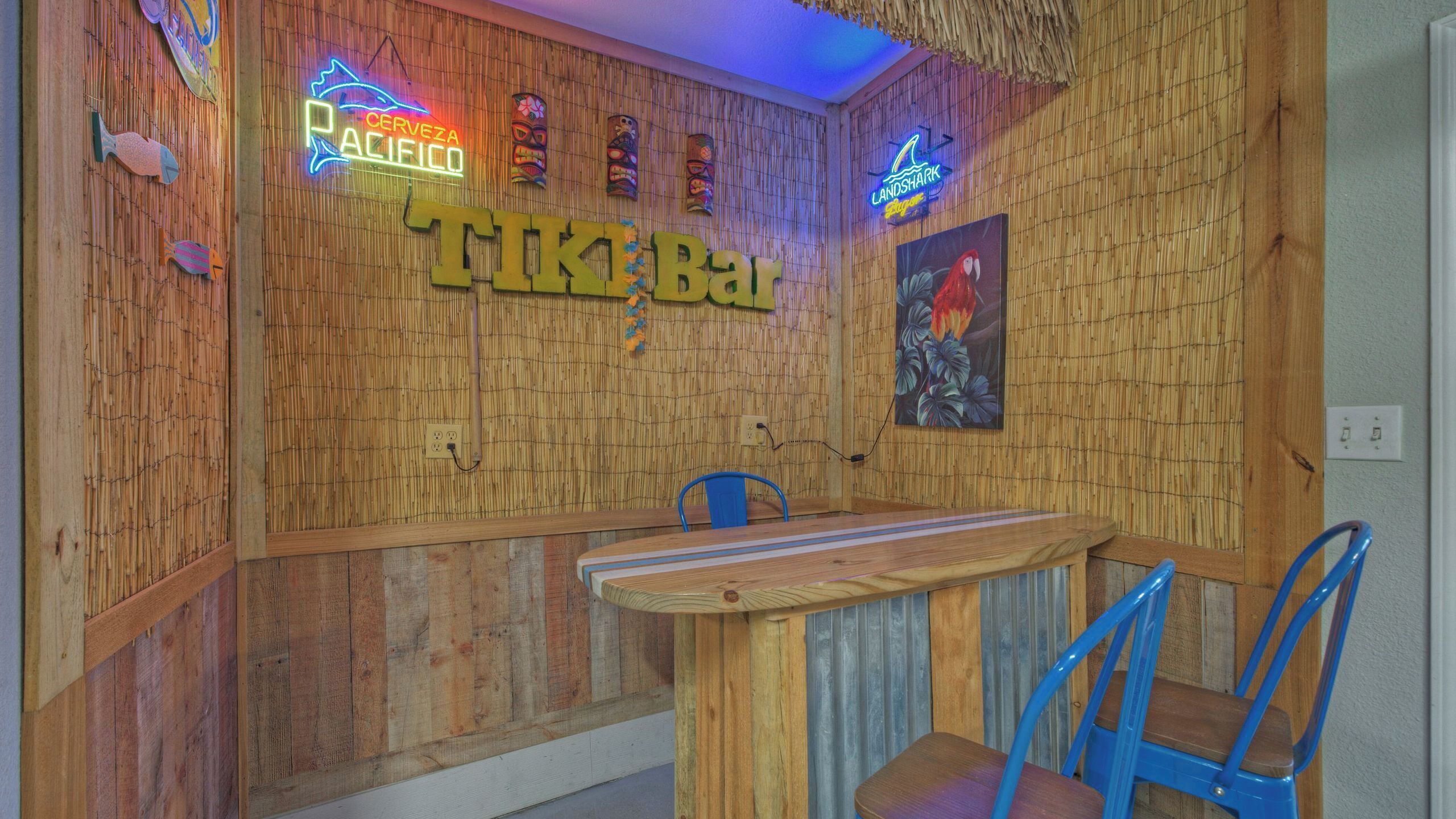 A tiki bar with a wooden wall, neon signs, and a parrot painting.