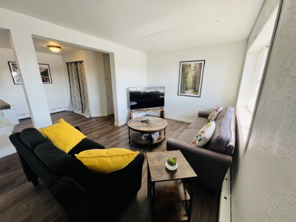 Ein Wohnzimmer mit einer schwarzen Couch, einem runden Couchtisch und einem Fernseher.