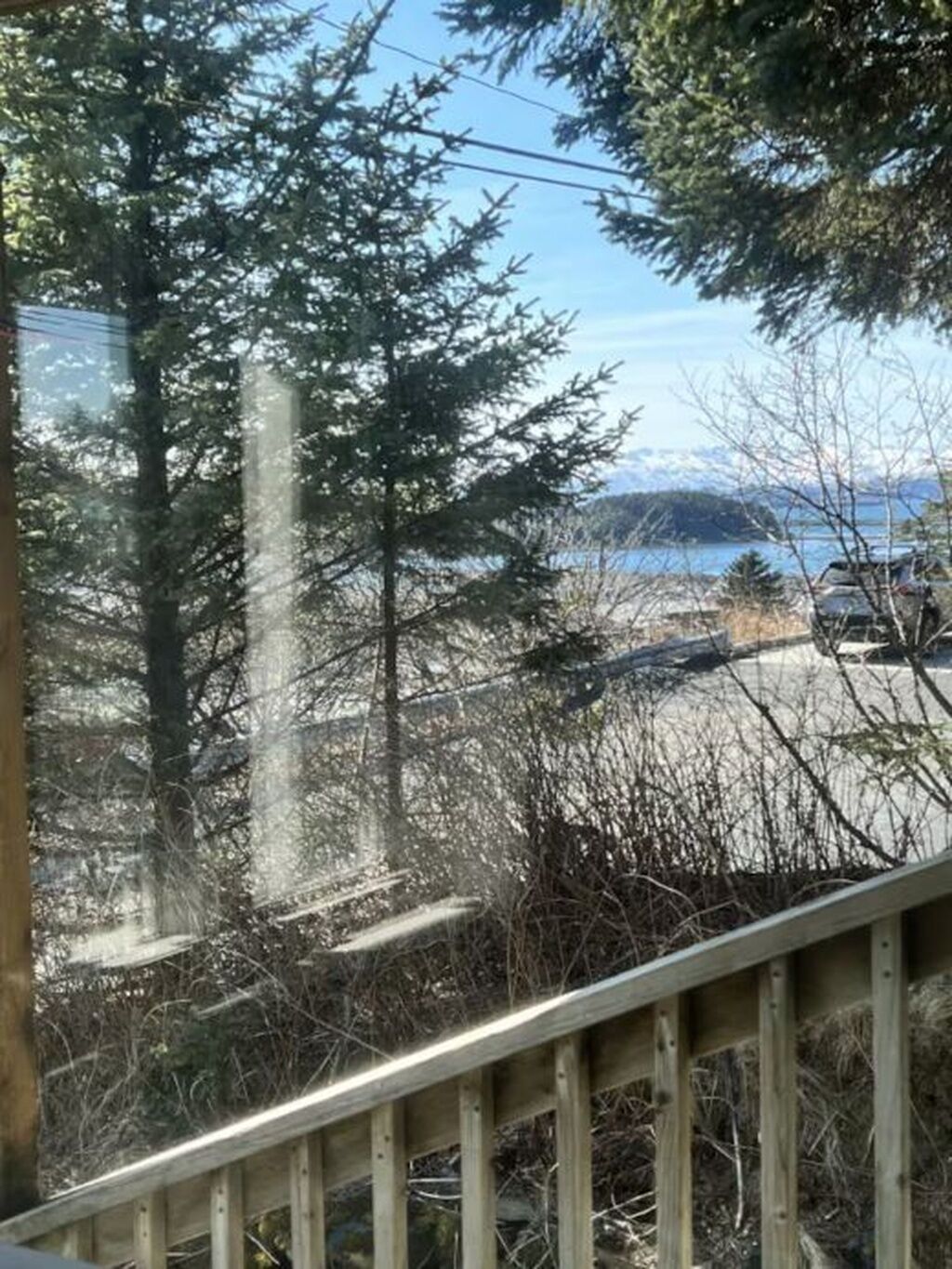 A view of a forested area with a wooden railing, a road, and a body of water in the distance.