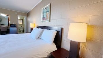 A hotel room with a large bed, bedside lamps, a framed picture on the wall, and a small desk with a chair.