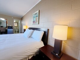 A hotel room with a large bed, bedside lamps, a framed picture on the wall, and a small desk with a chair.