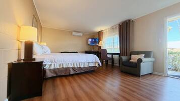A hotel room with a bed, a desk with a chair, a TV, and a view through a window.