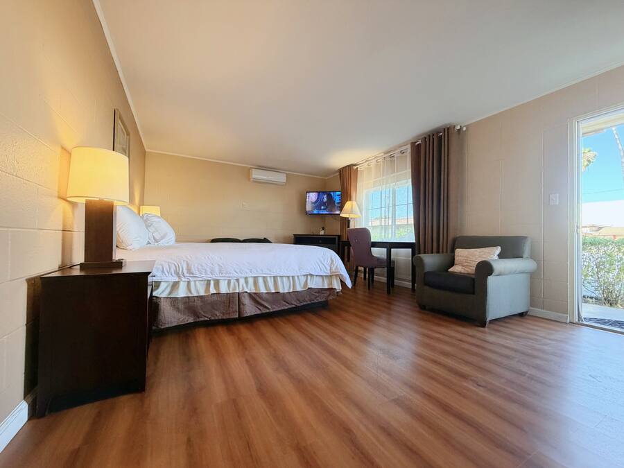 A hotel room with a bed, a desk with a chair, a TV, and a view through a window.