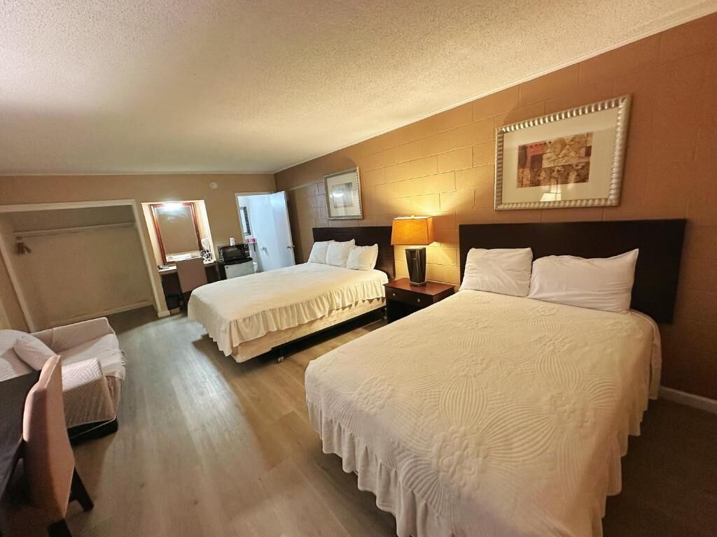Una habitación de hotel con dos camas, un escritorio, una silla y un espejo.