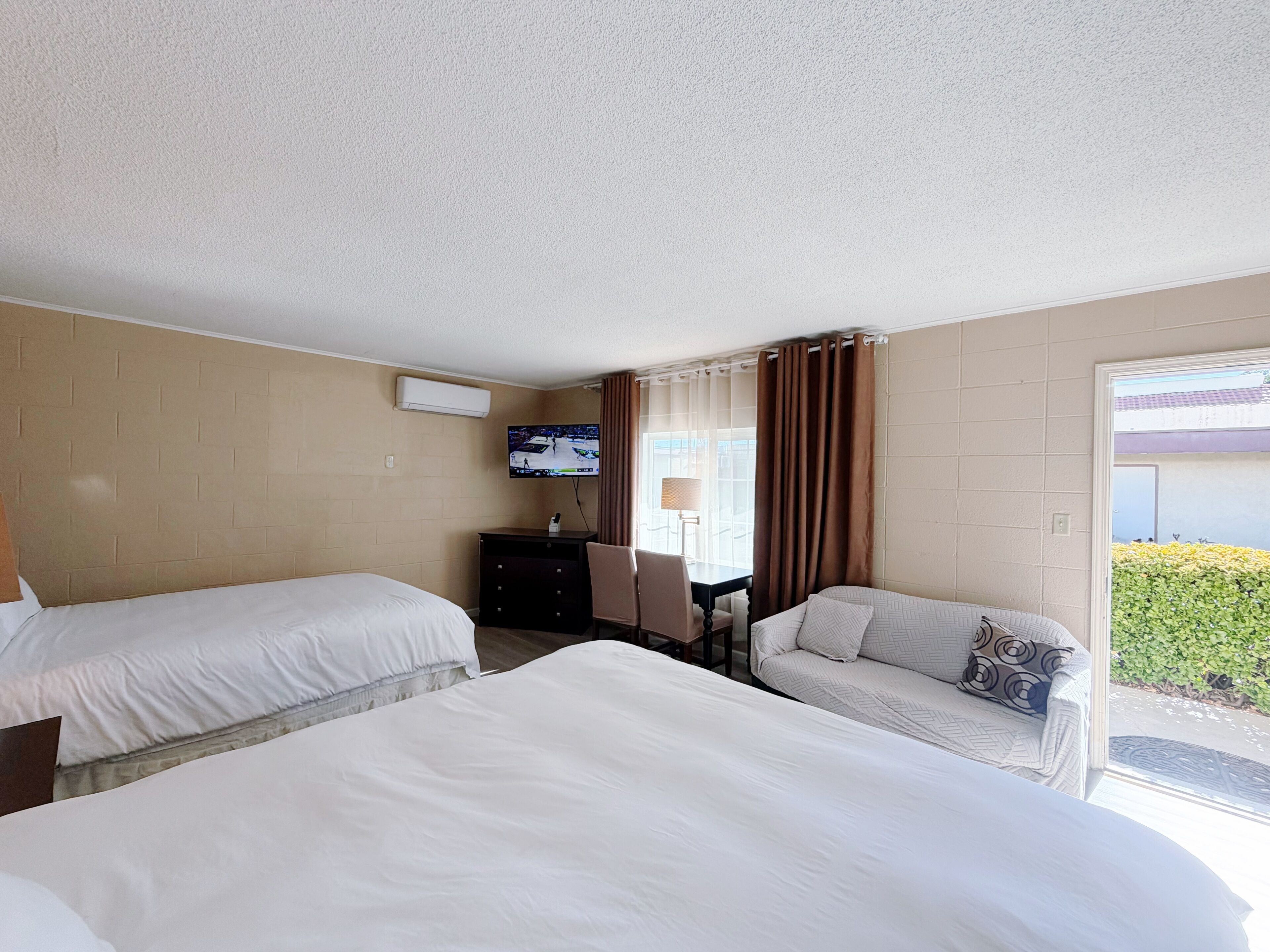 A hotel room with two beds, a desk, a chair, a TV, and a window with curtains.