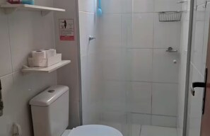 Ein Badezimmer mit Toilette, Duschkabine und Ablage für Toilettenpapier.