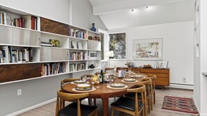 A dining area with a wooden table set for six, surrounded by bookshelves filled with books and decorative items.