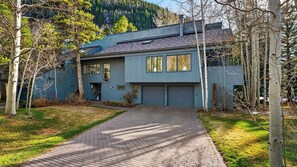 A two-story house with a garage, surrounded by trees and a mountain in the background.