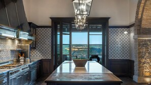 A kitchen with a large island, dark cabinetry, and a view through large windows.