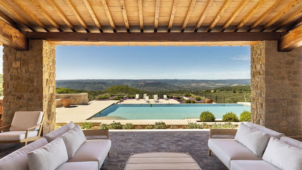 A stone-walled outdoor seating area with a pool and a view of a mountainous landscape.