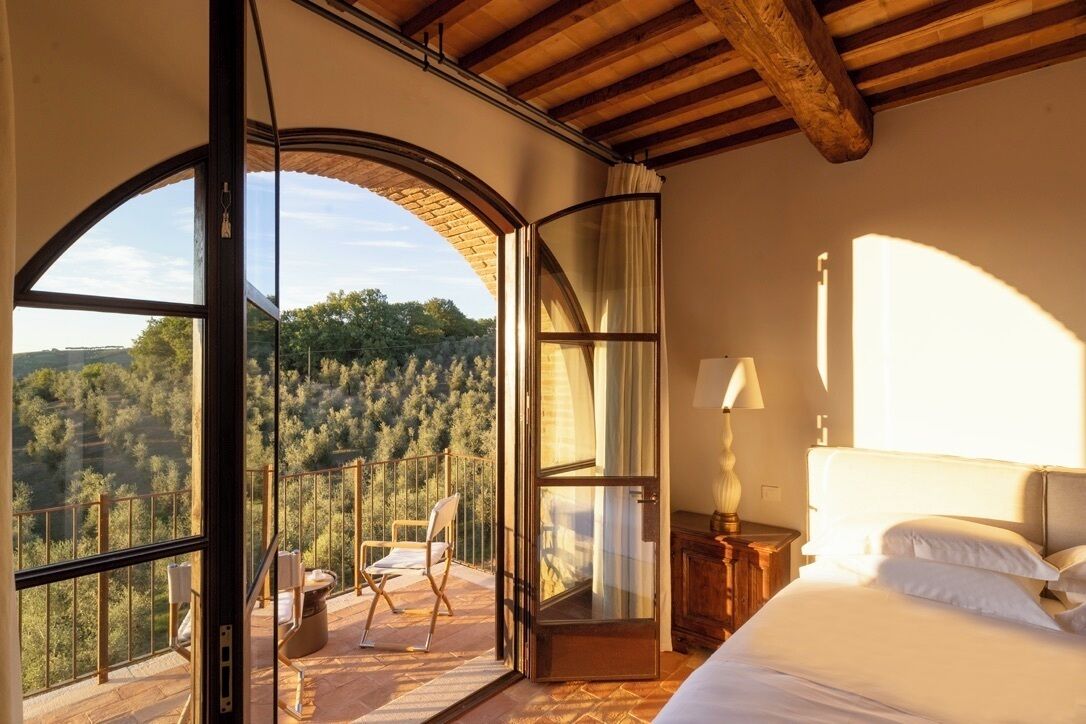 A bedroom with a large window, a bed, a nightstand, and a chair.